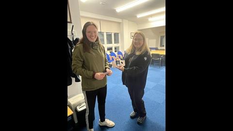 Two women, one handing over a pager to the other inside a lifeboat station
