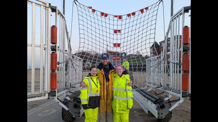 Faye, Lisa and Ben pose, smiling, in front of a recovery net fully rigged inside the recovery carriage for the RNLI.
