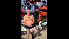 Dave is sat on the trailer with the orange lifeboat behind him.