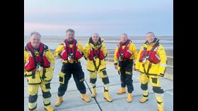 Memebers of Wells RNLI lifeboat crew in full inshore and all-weather lifeboat kit on the slipway at Wells Station, beach is in the background