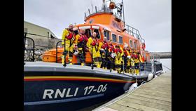 Ten crew in drysuits and lifejackets lined up on the deck of the Aran ALB which is tied up at a pontoon