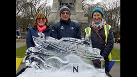 Three people stand behind an ice sculpture of a Shannon class Lifeboat