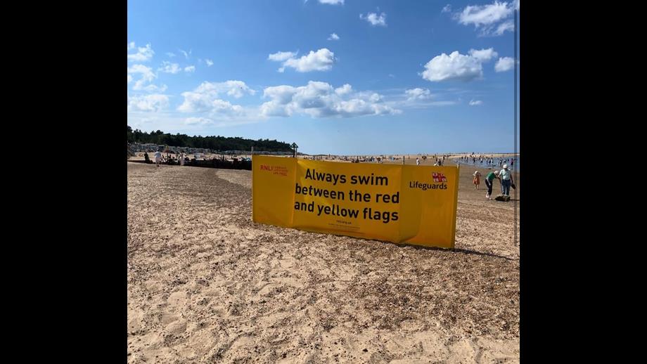 Always swim between red and yellow flags sign on Wells beach. Trees and beach huts in back round on a sunny summers day