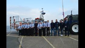Crew members standing infront of orange lifeboat holding their medals, deputy lord leitantant and RNLI Area Operations Manager also stood with crew members

