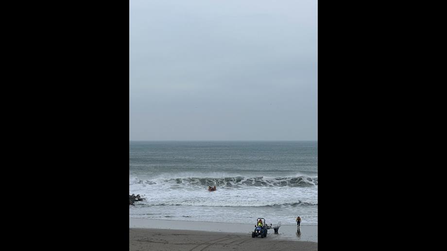 A D-class lifeboat approaches the beach in surf while a tractor and trailer await.
