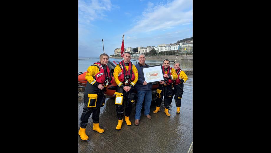 Malcolm handing over his painting to Weston crew by Marine Lake in front of the D Class lifeboat