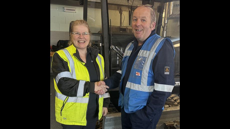 Caroline Jones on the left wearing RNLI high vis jacket, shaking hands with Simon Bunting, RNLI assessor. They are standing in front of a ToolTrack tracked launch vehicle.
