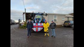 Photo of tractor with RNLI coxswain and two volunteer with RNLI flag