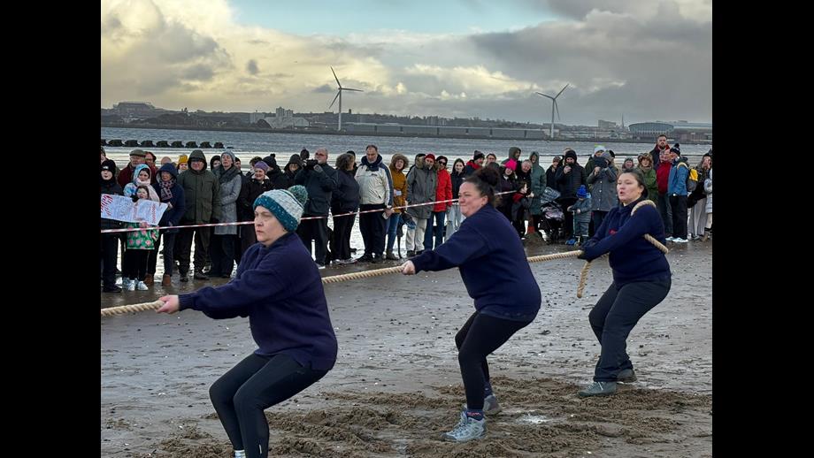New Brighton beach. Three of New Brighton's women's team can be seen pulling hard on the tug of war rope. Behind the crowds of spectators can be seen watching on.