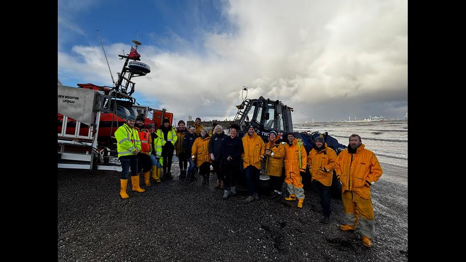 New Brighton RNLI volunteers pose for a group photo, in their yellows, in front of the tractor, lifeboat and carriage, on New Brighton beach.