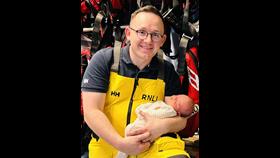 Photo of a smiling dad in RNLI yellow kit with his new baby 