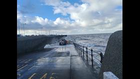Photo looking down Portland slipway in New Brighton. At the bottom, entering the water, can be seen the tractor, carriage and lifeboat. A lot of white water and breaking waves show it is rough conditions for launch.