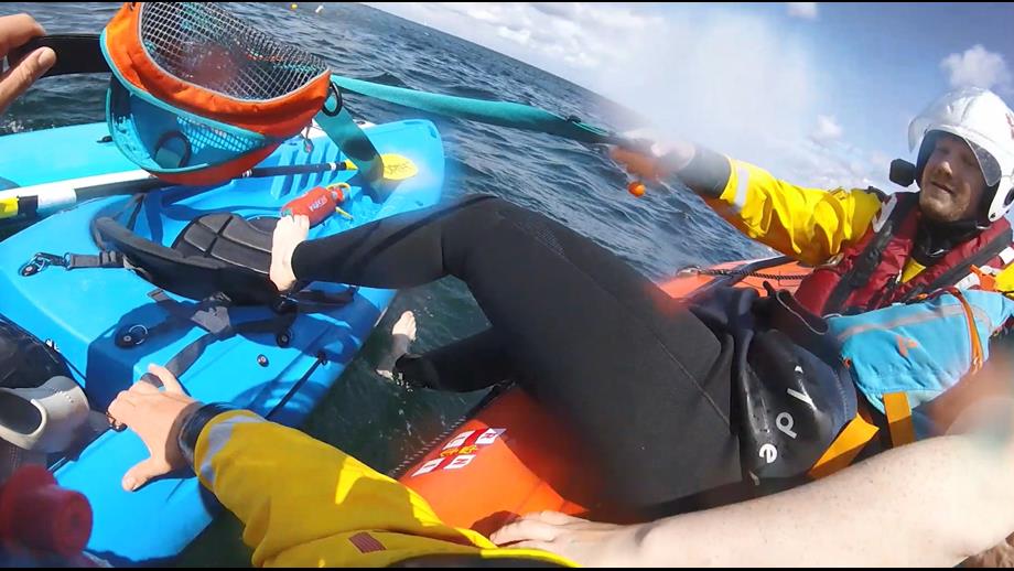 RNLI crews assisting a person from a kayak after being blown offshore