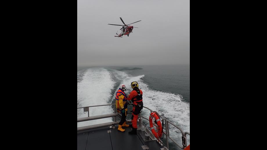 Crew members on the back of the boat with the helicopter in the background.