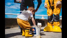 Child in yellow wellies placing donation into donation bucket