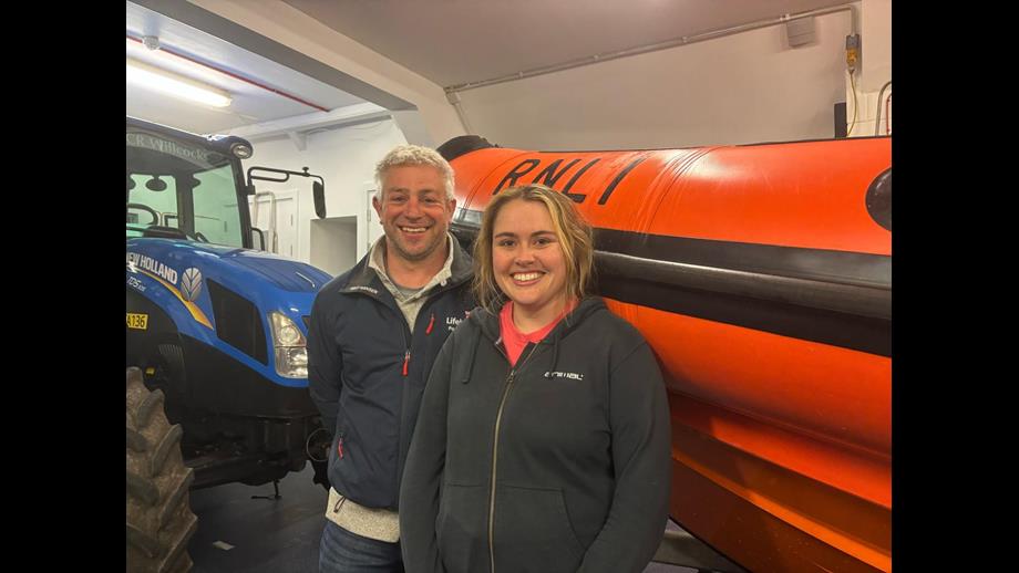 Two lifeboat crew members standing in front of a lifeboat and tractor