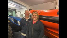 Two lifeboat crew members standing in front of a lifeboat and tractor