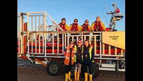 New Brighton RNLI's all-female launch crew pose with their Atlantic-85 lifeboat, on the carriage. Some crew are on board, some are stood on the ground.