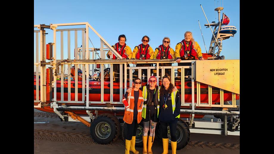 New Brighton RNLI's all-female launch crew pose with their Atlantic-85 lifeboat, on the carriage. Some crew are on board, some are stood on the ground.