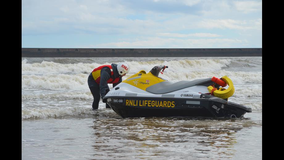 Lifeguard Supervisor Training with jet-ski at Roker Sunderland. liefguard in full RNLI lifeguard kit with RNLI jet ski on shore in the Surf. Sea and breaking waves in background
