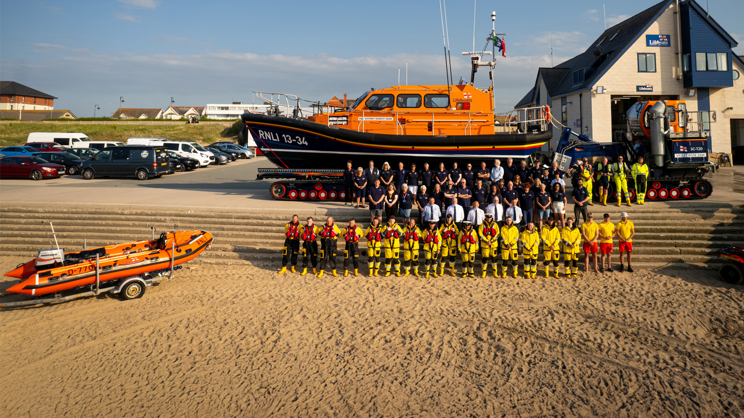 Rhyl crew standing in front of lifeboat on beach, in front of lifeboat station