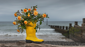 RNLI rose With Courage in a yellow welly on the beach