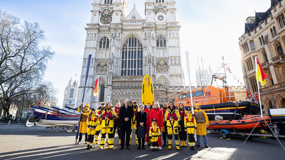A group of RNLI people outside Westminster Cathedral in London with a historic and two modern lifeboats and a lifeguard rescue board