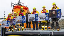 RNLI volunteers, some in crew kit, standing on an all-weather lifeboat holding large pictures of Guernsey Post’s commemorative RNLI 200th anniversary stamps