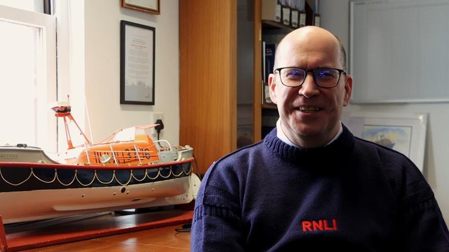Head and shoulders shot of Anstruther RNLI Crew Member Richard MacDonald sitting next to a model of a historic RNLI lifeboat   