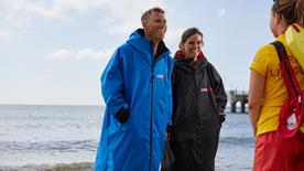 Man and woman in dryrobes smiling at an RNLI LIfeguard