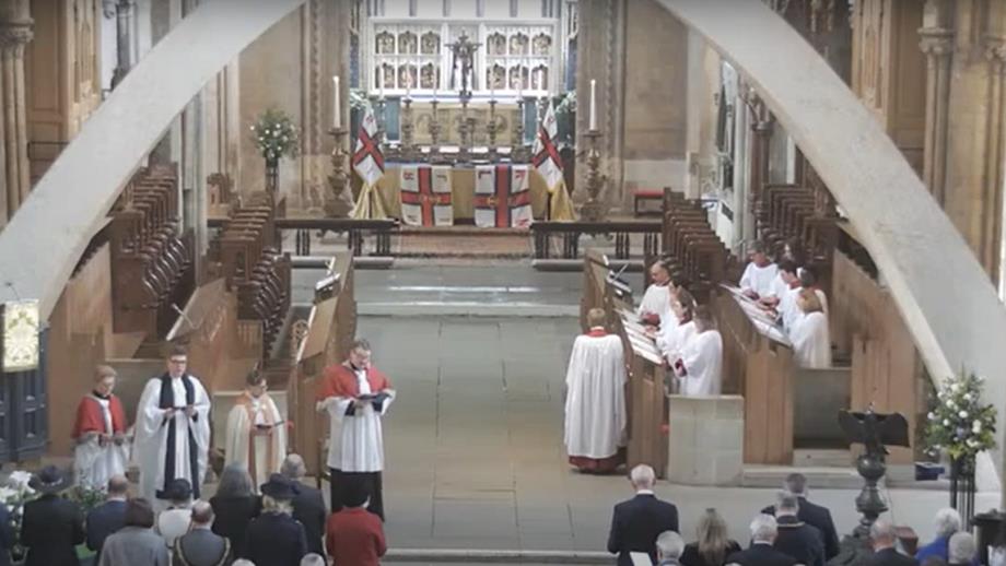 Inside Llandaff Cathedral during the RNLI Service of Thanksgiving on 27 April 2024. The clergy, choir and people in pews are standing and RNLI flags adorn the altar. 