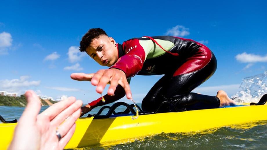 An image of an RNLI lifeguard reaching towards the hand of a person in the water, taken from the point of view of the person in the water.