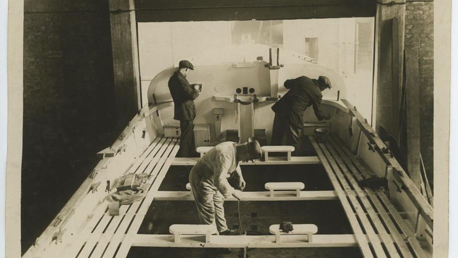 Black and white image of three men working on lifeboat inside depot