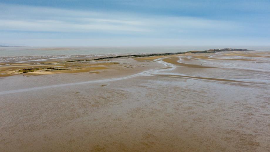 Aerial view of a beach with water, showcasing Hilbre Island becoming cut off by the rising tide.