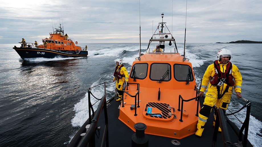 A Severn class lifeboat and a Shannon class lifeboat are side-by-side on a calm sea, with lifeboat crew members stood on the bows