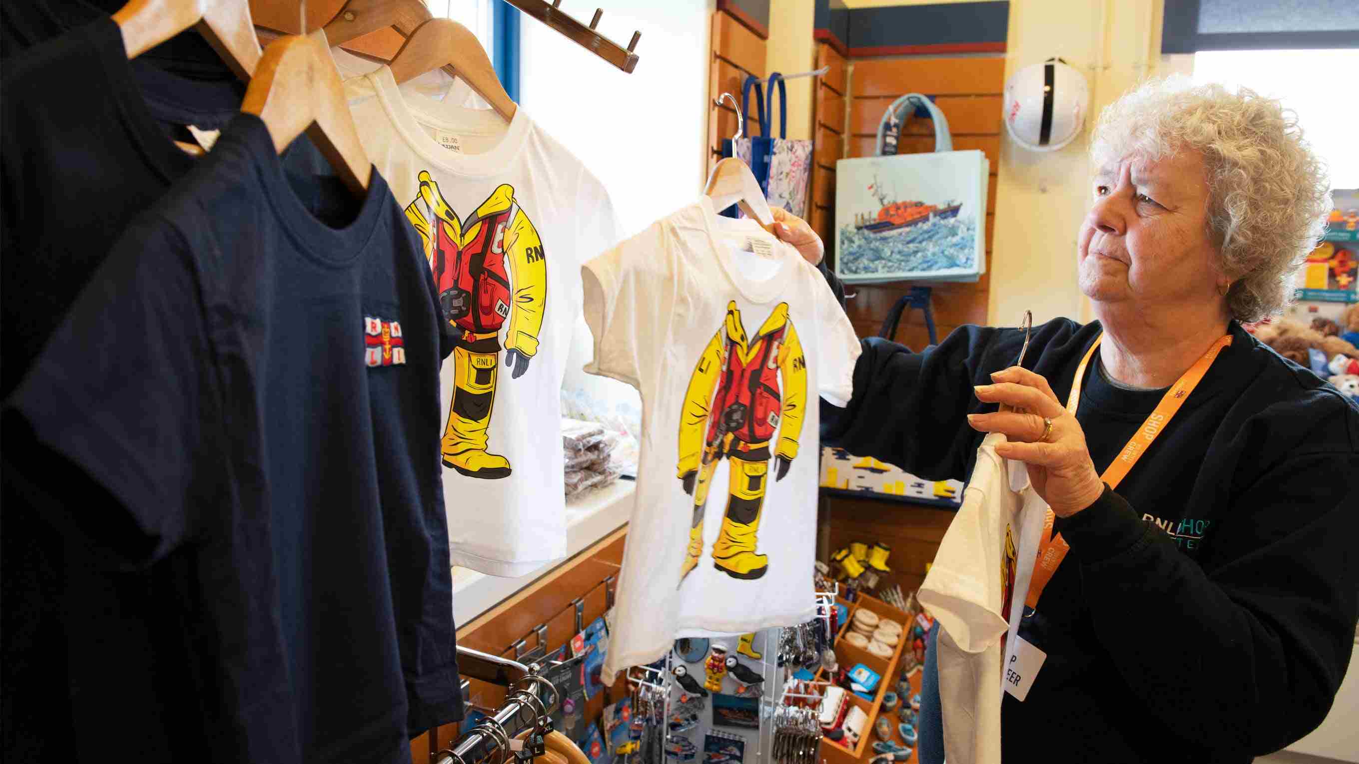 A Barrow RNLI shop volunteer hangs a branded T shirt on a hook onto a rack of clothes 