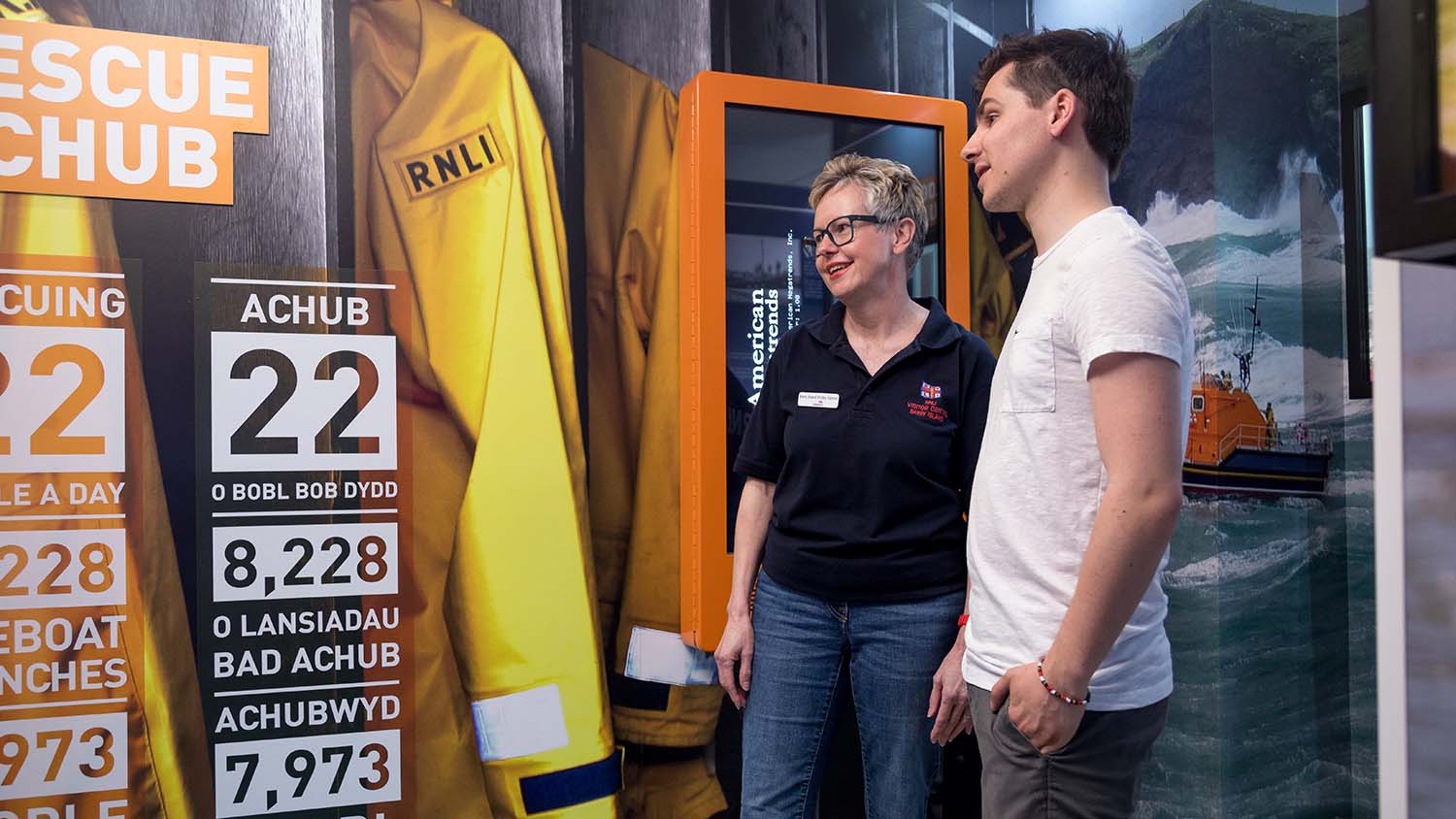 A female RNLI volunteer talking to a member of the public in front of an informative display.
