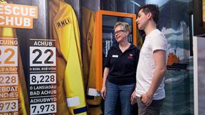 A female RNLI volunteer talking to a member of the public in front of an informative display.