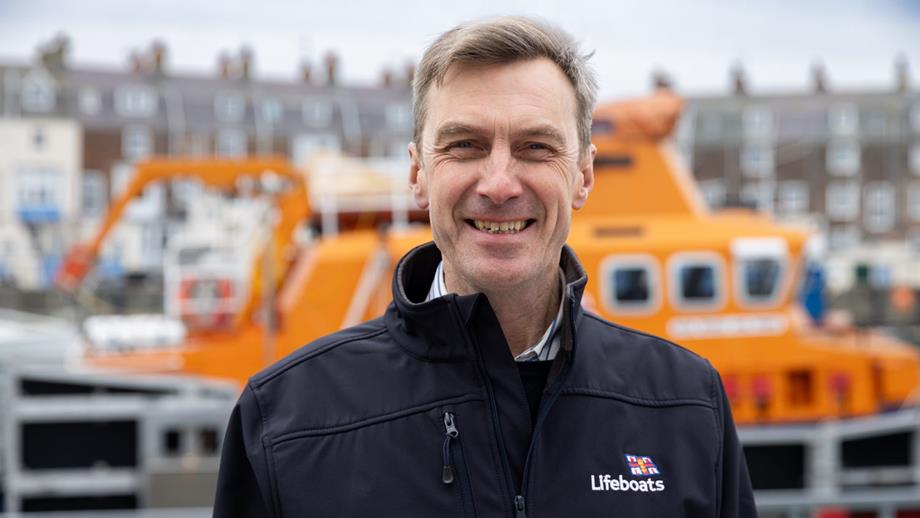 Smiling headshot of Peter Sparkes, RNLI CEO, standing in front boat in black jacket.