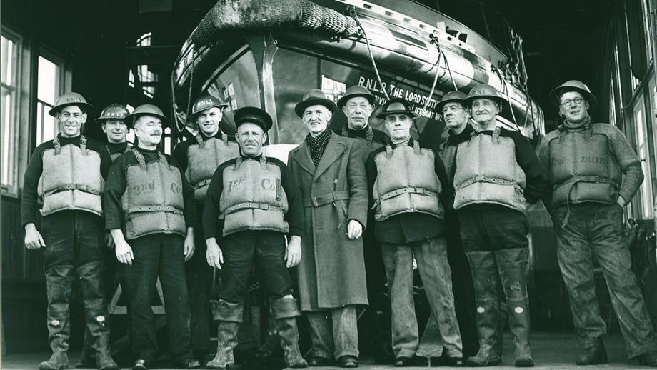RNLI lifesavers during the Second World War. They are smiling at the camera and standing in front of a lifeboat.