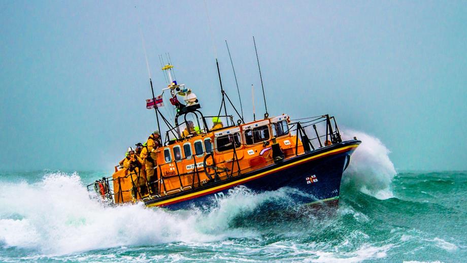 A Mersey class lifeboat breaking through the swell. The wake is breaking around the sides of the boat and the sky is hazy.