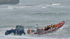 A lifeboat with four crew members is being launched into the sea by a tractor.