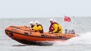 Four RNLI crew members dresses in yellow suits on an orange, open top lifeboat on the water.
