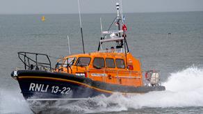 An orange and dark blue RNLI lifeboat powers through grey, choppy waters.