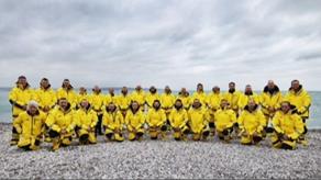 Image of Torbay crew stood on a beach facing the camera with backs to the sea, wearing yellow kit