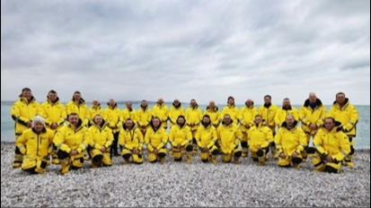 Image of Torbay crew stood on a beach facing the camera with backs to the sea, wearing yellow kit