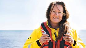 A female lifeboat crew member wearing all-weather lifeboat kit smiles for the camera next to the sea
