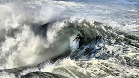 A surfer in a winter wetsuit with hood surfing a big wave