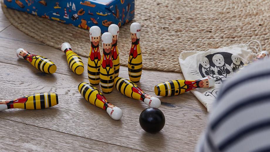 A set of 10 bowling pins with two black boules next to them. Each of the pins are painted as an RNLI lifeboat crew member in full kit. 