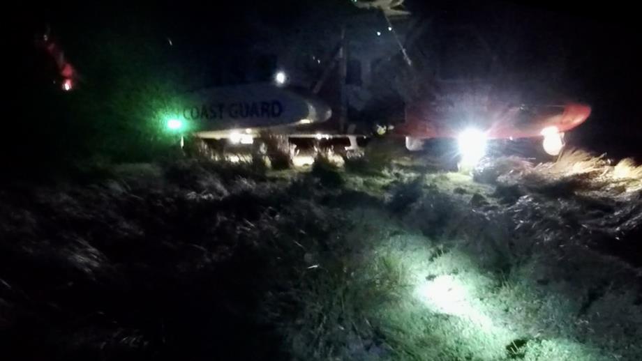 A Coast Guard rescue helicopter that has landed at night-time on uneven, grassy ground.
